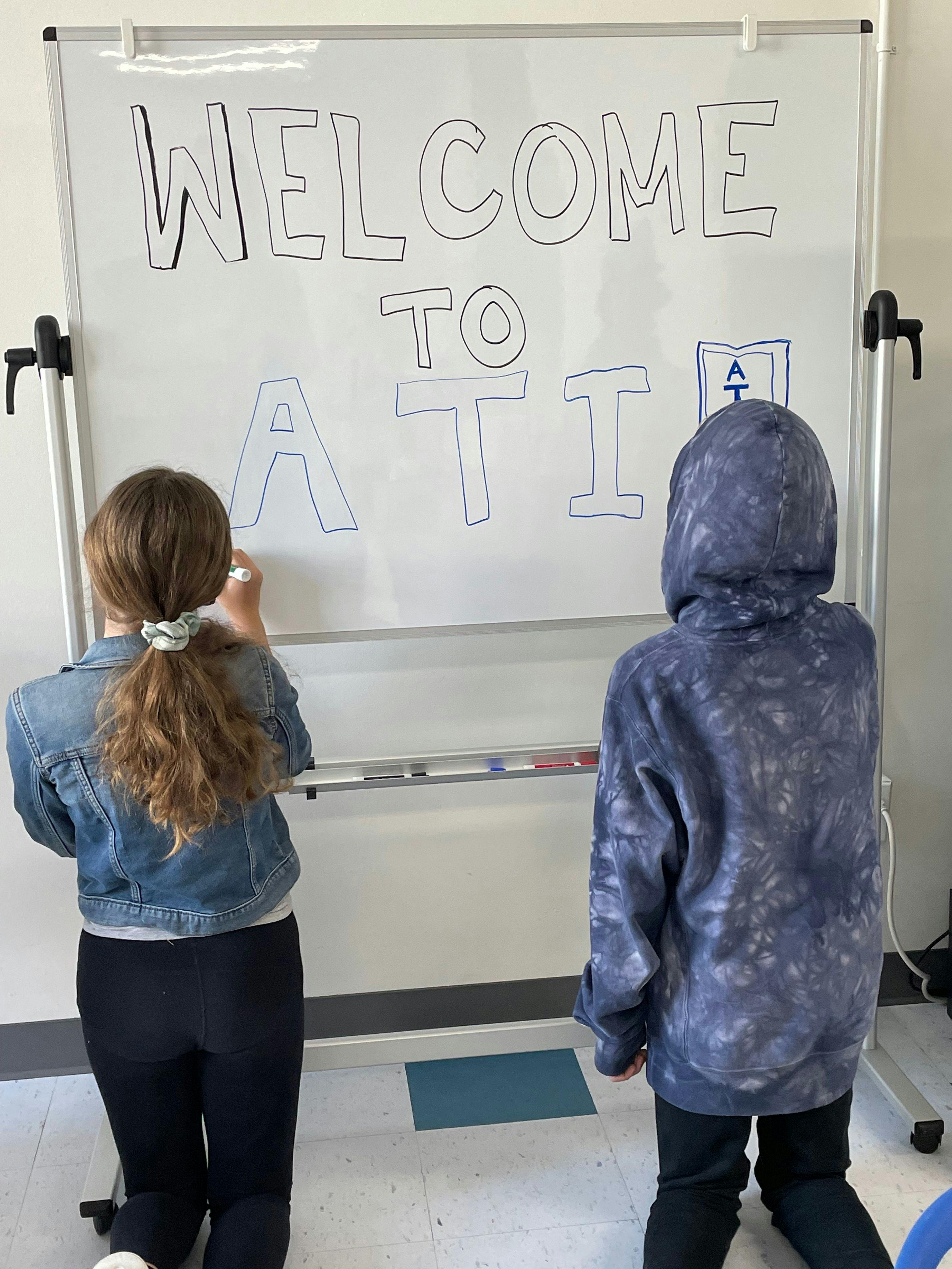 two ati chantilly students writing welcome to ati on whiteboard